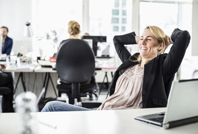 Relaxed mid adult businesswoman looking away while reclining at desk in office