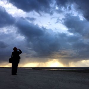 Rear view of man standing by sea against cloudy sky