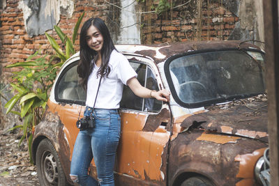 Portrait of young woman smiling while standing by abandoned car