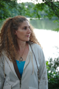 Mature woman looking away while standing against lake