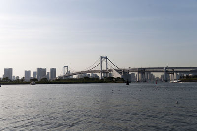 Rainbow bridge over tokyo bay in city against clear sky