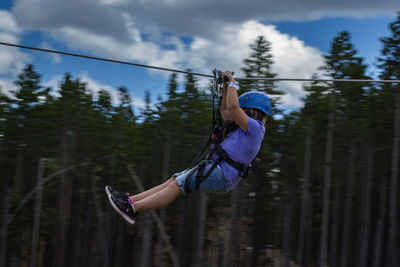 Girl ziplining against cloudy sky