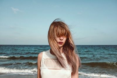 Beautiful woman with tousled hair standing on sea shore against sky