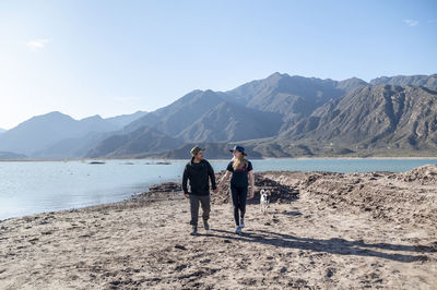 Couple holding hands while walking outdoors with natural landscape of mountains and lake.