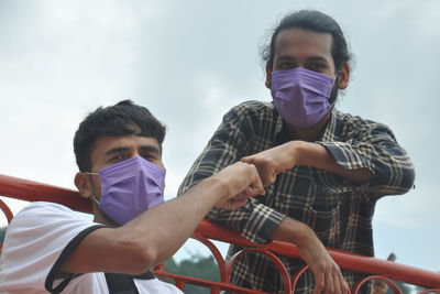 Two male friends wearing face mask with making fist bump in outdoor while looking at camera