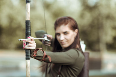 Portrait of archer holding bow and arrow standing on field