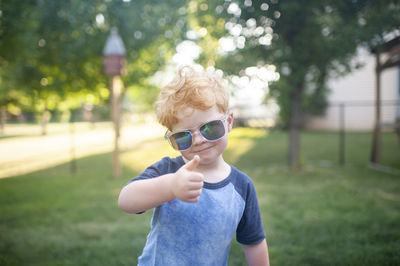 Young boy giving a thumbs up with sunglasses on standing in backyard