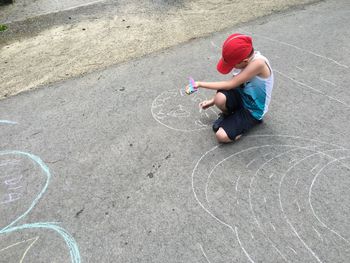 High angle view of boy drawing with chalk on footpath