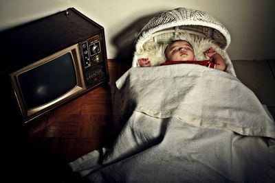 High angle view of baby boy sleeping in crib by television set