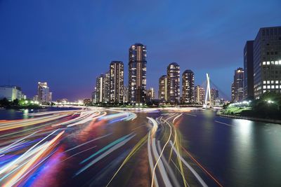 Light trails on road in illuminated city at dusk