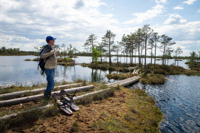 A tourist stands near a lake among a raised bog, nearby there are devices for walking in the swamp