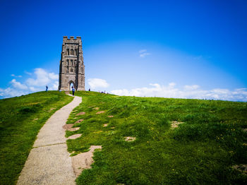 Glastonbury tor tower, clear blue sky, green grass, winding path.
