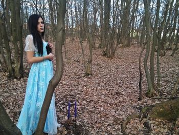 Smiling young woman standing by bare trees in forest