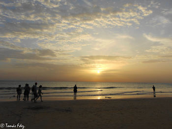 Silhouette people standing on beach against sky during sunset