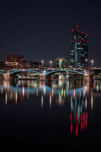 Illuminated bridge over river by buildings against sky at night