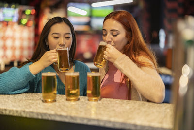 Multiracial women drinking beer at bowling alley
