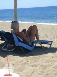Woman sitting on chair at beach against sea