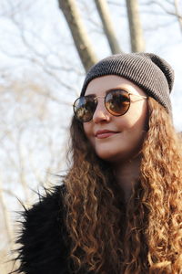 Woman wearing sunglasses against bare trees