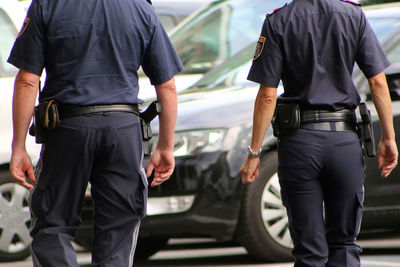 Midsection of security guard walking against cars