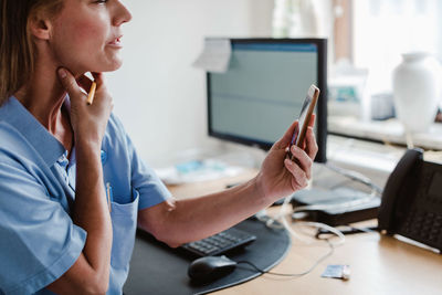 Female pediatrician using smart phone while explaining through video conference in office