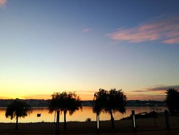 Silhouette trees by lake against sky during sunset