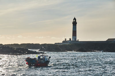 Lighthouse on sea against sky during sunset