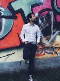 Full length of young man standing against graffiti wall