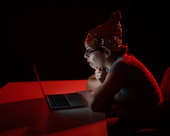 Side view of young woman using mobile phone while sitting against black background