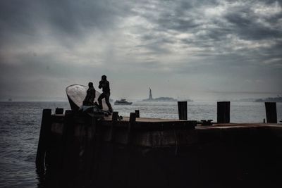 Silhouette men standing on sea against sky