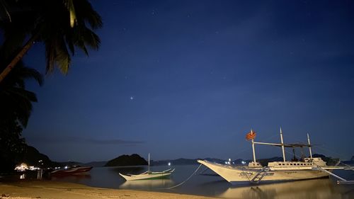 Sailboats moored on sea against sky at night