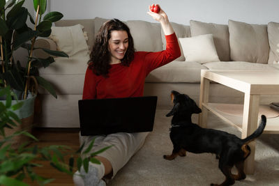 Portrait of young woman with dog sitting on sofa at home