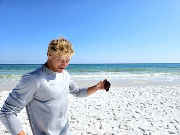 Young man millennial leaving sandy beach on vacation holding his cellphone.