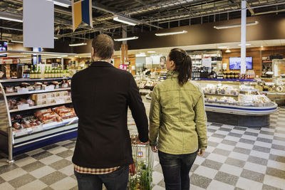 Rear view of couple walking with shopping cart at grocery store