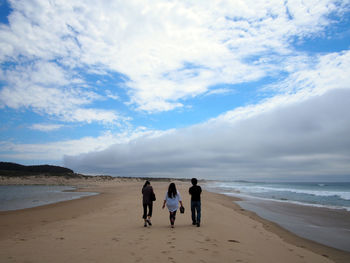 Rear view of men walking on beach against sky