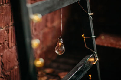 Close-up of illuminated light bulb hanging against wall