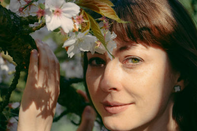 Close-up portrait of beautiful woman standing by white blossoms on sunny day