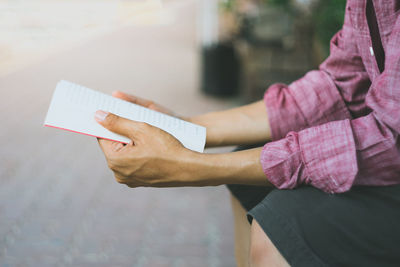 Midsection of man reading book while sitting outdoors