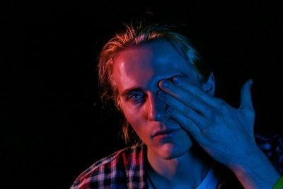 Portrait of man with eye covered by hand in darkroom