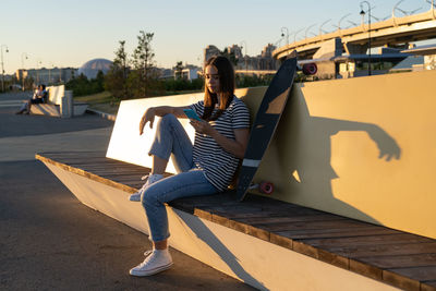 Young girl use smartphone outdoors at urban park chatting with friends in mobile phone messenger