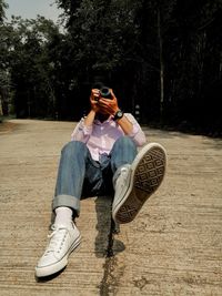 Full length of man using camera while sitting on the road 