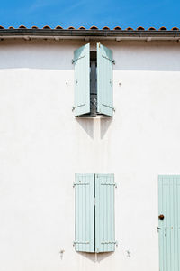 Windows with wooden light green painted closed shutters in white wall in old house