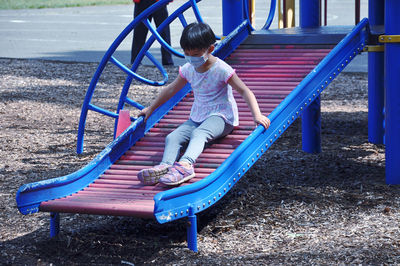 Full length of girl sitting on slide at playground