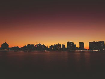 Silhouette buildings by river against sky during sunset