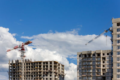 Building process of large residential apartment building with crane on cloudy sky background