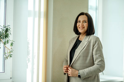 Smiling business. smiling businesswoman. entrepreneur stands in jacket in office lobby by the window