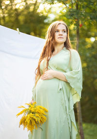 Pregnant woman with big belly, yellow goldenrod solidago flowers in hands. white female wears dress