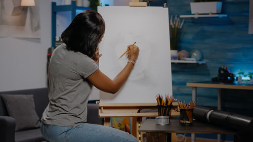 Side view of young woman painting at home