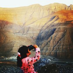 Girl looking through binoculars against mountain