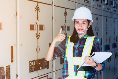 Portrait of woman gesturing while standing by electrical fuse