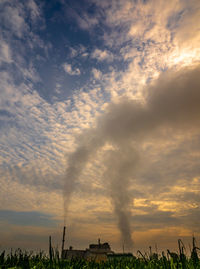 Smoke emitting from chimney on field against sky during sunset